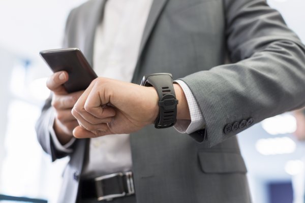 man in suit checking time smartwatch holding smartphone